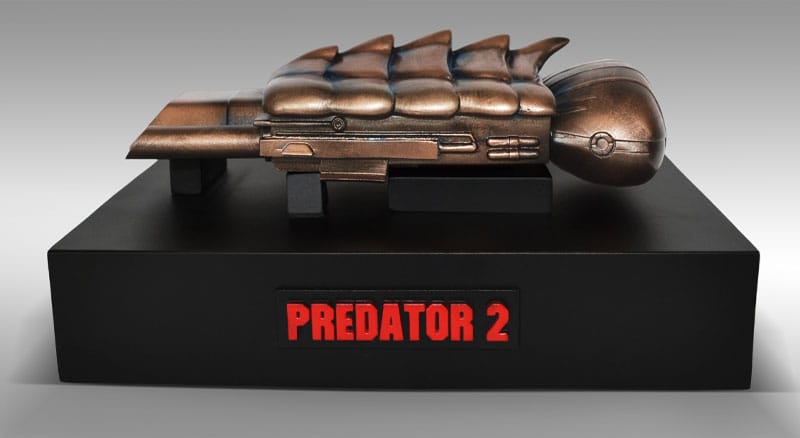Vista superior del Plasmacaster de Predator 2 sobre base decorativa con logo